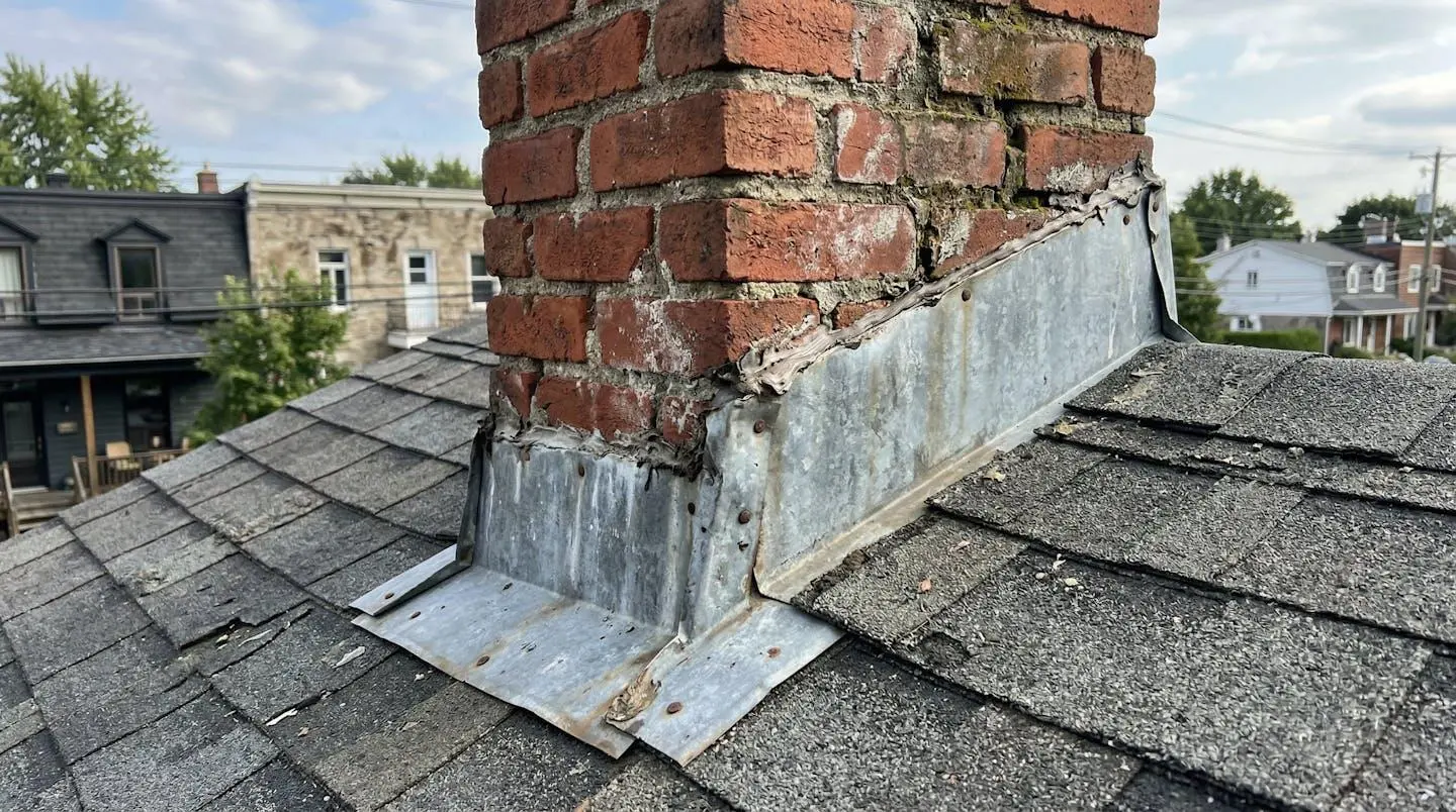 Gros plan sur la zone de raccord entre une toiture en bardeaux et une cheminée en brique, montrant l'installation du solin métallique