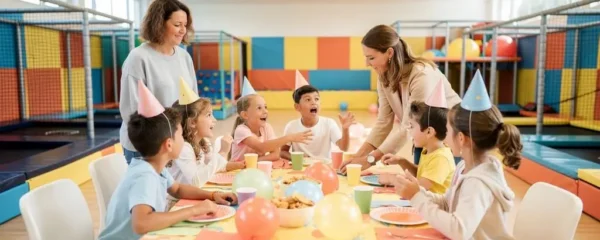 Des enfants fêtent un anniversaire autour d'une table décorée dans la zone dédiée d'un parc de loisirs indoor, avec des structures de jeu en arrière-plan.